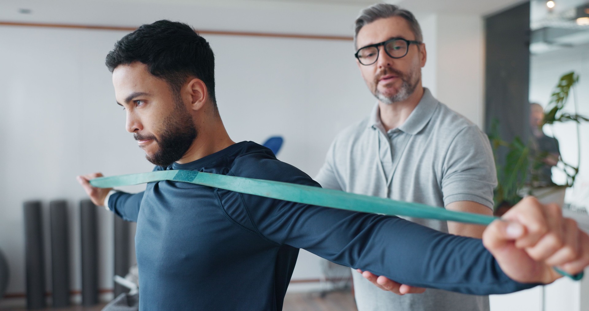 Physiotherapy, resistance band and consulting with man and athlete in clinic for rehabilitation, healthcare or stretching. Support, medical and muscle with people for healing, advice or recovery